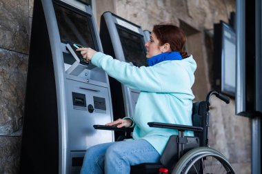 Tekerlekli sandalyedeki beyaz bir kadın, bir self-servis kasasında cep telefonu kullanarak tren bileti alıyor.. 