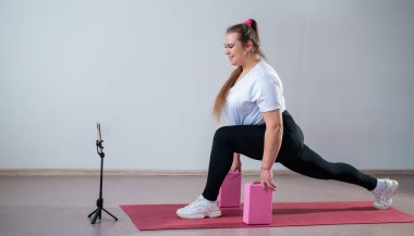 Genç Artı Boyutlu Kadın İnternet 'te esniyor. Esnek kız yoga yapıyor ve internetten dizüstü bilgisayarda ders izliyor.