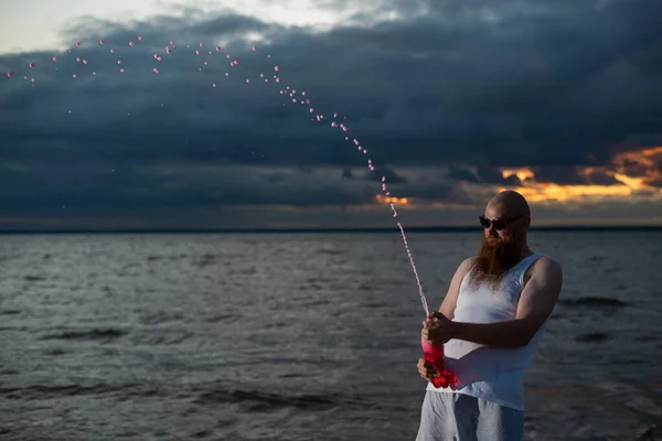 Un ritratto umoristico di un uomo brutale che versa soda da una bottiglia sulla spiaggia al tramonto — Foto Stock