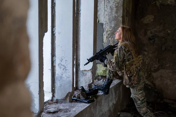 Una mujer con uniforme del ejército apunta a disparar un arma de fuego en un edificio abandonado. —  Fotos de Stock