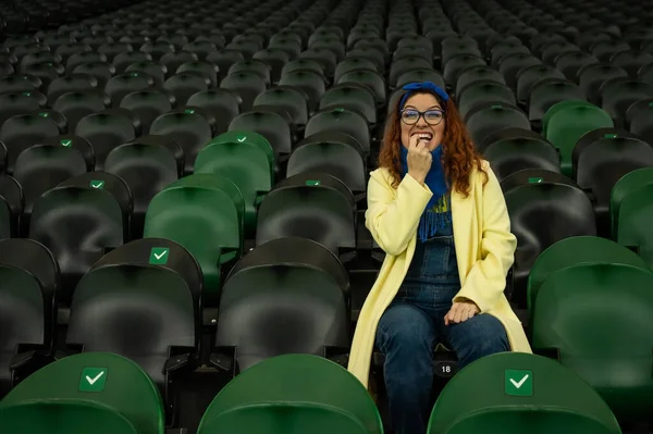Caucasian woman cheers for a sports team at the stadium. The girl watches the match at the stadium alone.