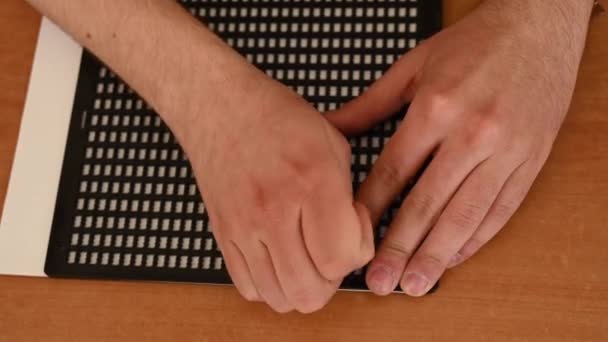 En man använder en speciell stencil och stylus för att skriva ett brev i blindskrift. — Stockvideo