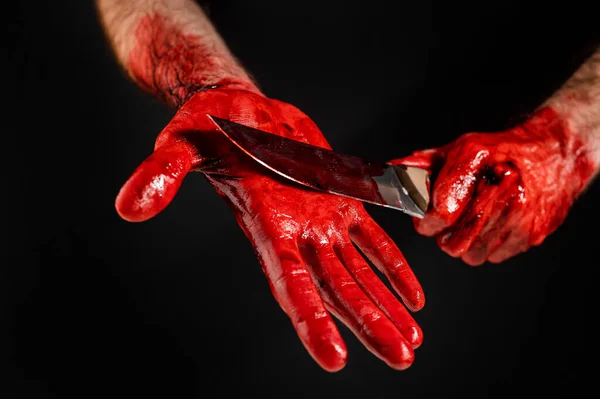Un hombre con las manos manchadas de sangre se corta la palma con un cuchillo sobre un fondo negro. — Foto de Stock