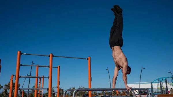 Shirless άνθρωπος κάνει handstand σε παράλληλα μπαρ στο γήπεδο του αθλητισμού. — Φωτογραφία Αρχείου