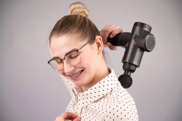 Lächelnde Frau mit Zahnspange benutzt Massagepistole für den Rücken. — Stockfoto