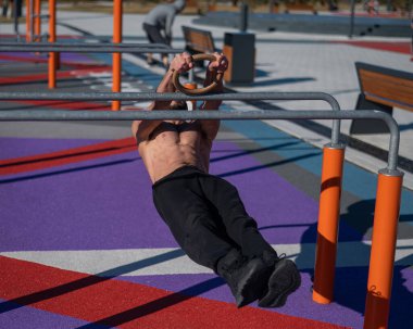 Spor sahasındaki paralel çubuklarda üstsüz adam yatay denge yapıyor.. 