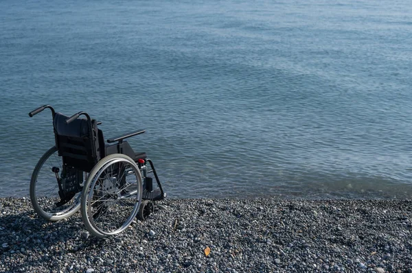 Una sedia a rotelle vuota su una spiaggia rocciosa. — Foto Stock