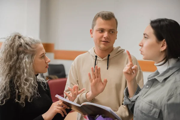Duas raparigas e um tipo falam em linguagem gestual. Três alunos surdos conversando em uma sala de aula universitária. — Fotografia de Stock