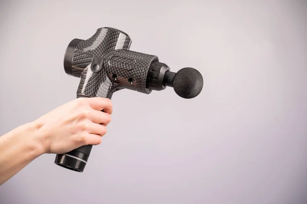 Närbild av en kvinnlig hand med en bärbar massagepistol på en vit bakgrund. — Stockfoto
