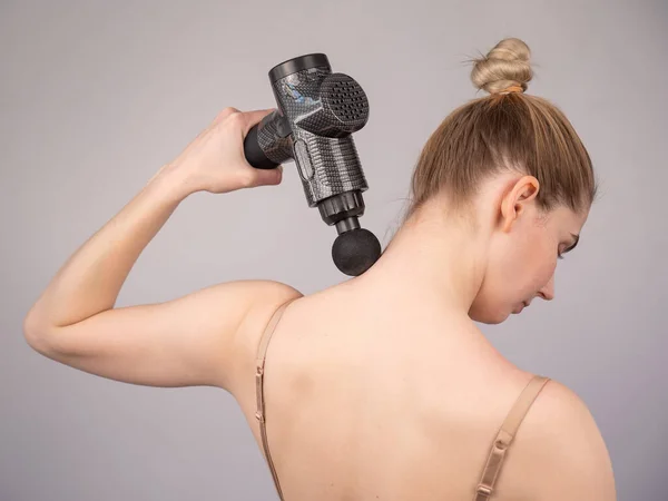 Caucasian woman giving herself a back massage with a gun. — Stock Photo, Image