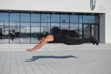 Siyah spor kıyafetli bir adam dışarıda şınav çekerken zıplıyor..