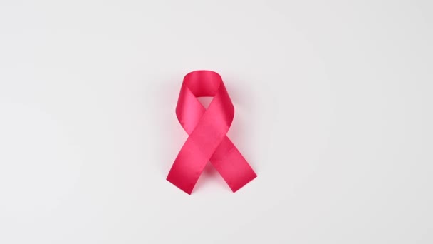 Een vrouw houdt een roze lint vast op een witte achtergrond. Symbool van de strijd tegen borstkanker. — Stockvideo