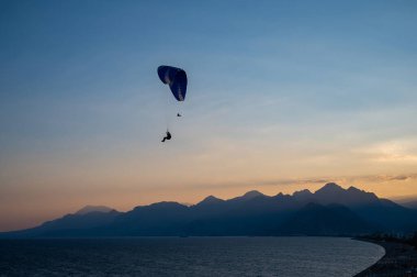 Gün batımında denizin üzerinde uçan bir adamın silüeti..
