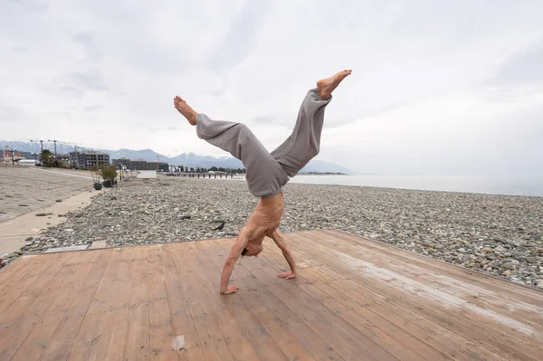 Póló nélküli fehér férfi csinál backflip kavicsos strand. — Stock Fotó