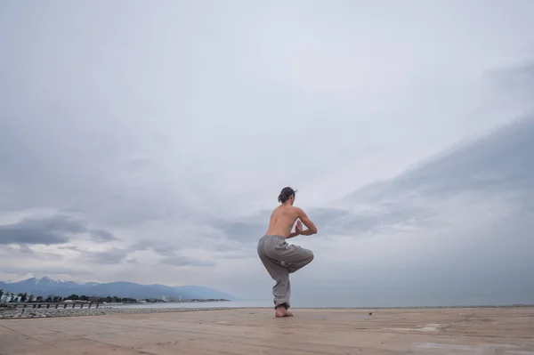 Beyaz bir adam, çıplak gövdesiyle deniz kıyısında wushu yapıyor.. — Stok fotoğraf