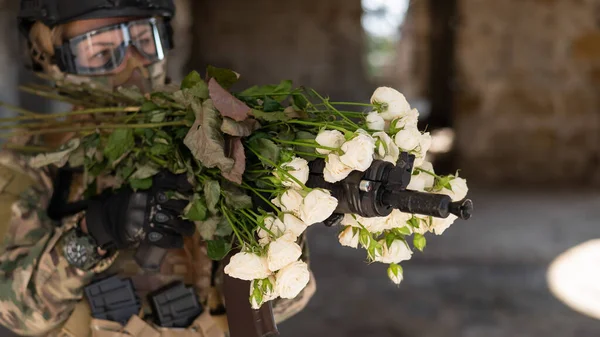Кавказка в военной форме держит пулемет и букет белых роз. — стоковое фото