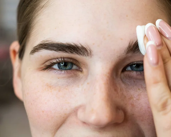 De master verwerkt de wenkbrauwen van een blanke vrouw met een wattenschijfje alvorens de wenkbrauwen te lamineren. — Stockfoto