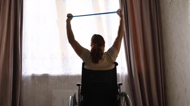 Mujer caucásica en silla de ruedas haciendo ejercicios con la ayuda de bandas de goma de fitness. — Vídeos de Stock