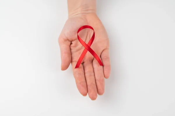 Kobieca dłoń z czerwoną wstążką na białym tle. Symbol walki z AIDS. — Zdjęcie stockowe