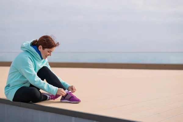 Mujer caucásica en sudadera con capucha atándose los cordones de los zapatos antes de correr. —  Fotos de Stock