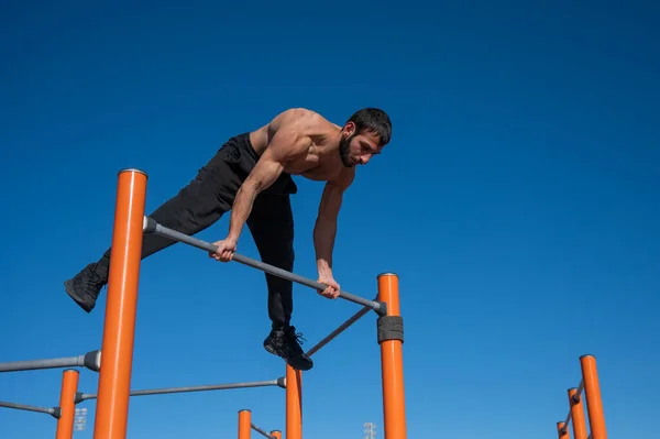 Egy férfi meztelen felsőtesttel egyensúlyt teremt a vízszintes korláton.. — Stock Fotó