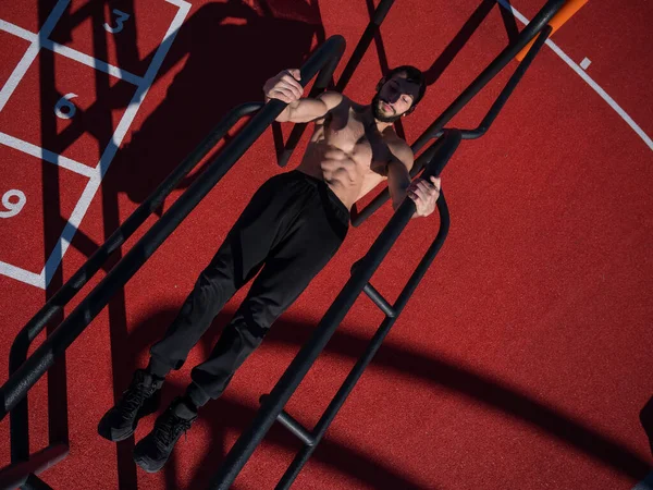 Un hombre sin camisa haciendo equilibrio en barras irregulares al aire libre. Vista desde arriba. — Foto de Stock