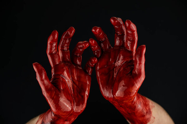 Womens hands in blood on a black background.