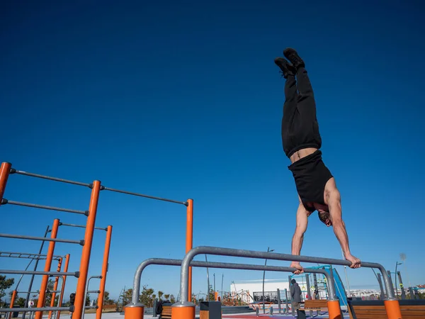 Uomo senza maglietta che fa manubrio su barre parallele al campo sportivo. — Foto Stock