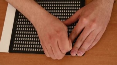 Bir adam körler alfabesiyle mektup yazmak için özel bir şablon ve stil kullanır.. 