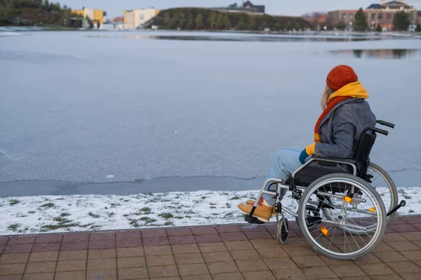 Vit kvinna i rullstol går vid sjön på vintern. — Stockfoto