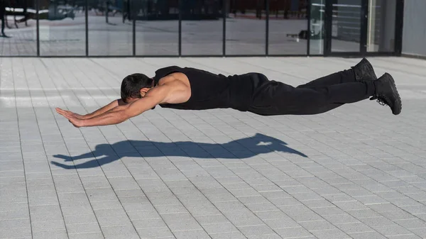Ein Mann in schwarzer Sportbekleidung springt beim Liegestützen im Freien. — Stockfoto