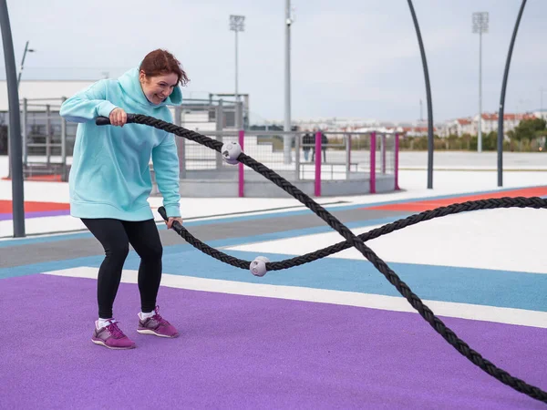 Кавказька жінка з м "ятного сорочку тренується з бойовими мотузками на спортивному майданчику.. — стокове фото