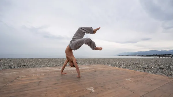 Shirtless Kaukasische man doet backflip op kiezelstrand. — Stockfoto