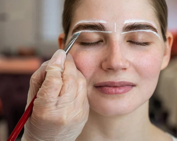 The master draws the shape of the eyebrows with white paint before coloring.