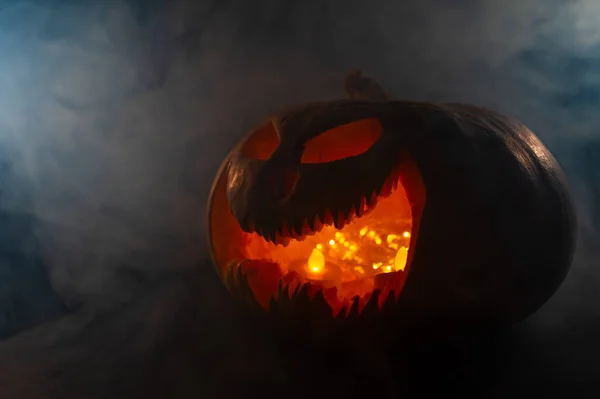 En läskig pumpa med en ristad grimace i röken. Jack o lykta i mörkret. — Stockfoto