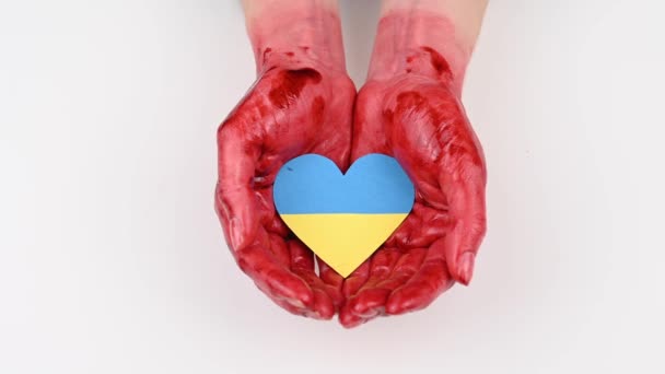 Una mujer cierra sus manos ensangrentadas sosteniendo un corazón con la bandera de Ucrania sobre un fondo blanco. — Vídeo de stock