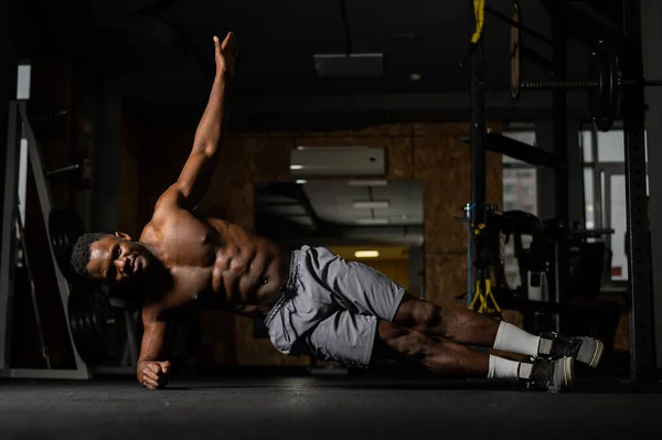 Félmeztelen afro-amerikai férfi csinál egy könyök oldalsó deszka az edzőteremben. — Stock Fotó