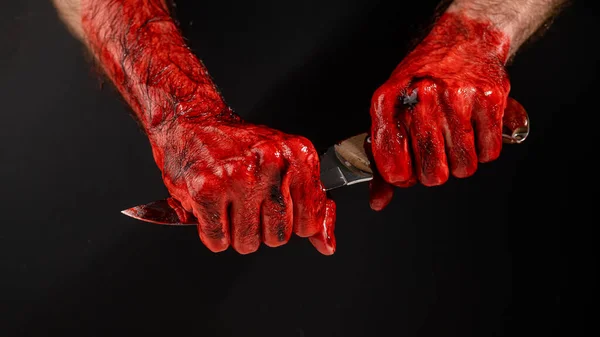 Un hombre con las manos ensangrentadas sostiene un cuchillo por la hoja sobre un fondo negro. — Foto de Stock