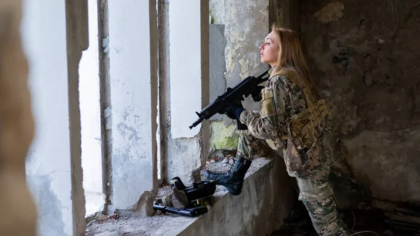 Una donna in uniforme militare mira a sparare a un'arma da fuoco in un edificio abbandonato. — Foto Stock