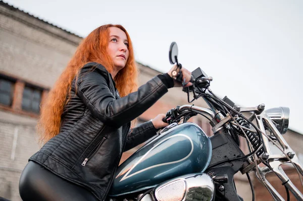 Femme bouclée aux cheveux roux en cuir vêtements moto en plein air. — Photo
