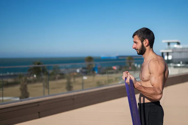 Hombre sin camisa haciendo ejercicio con bandas de goma al aire libre. — Foto de Stock