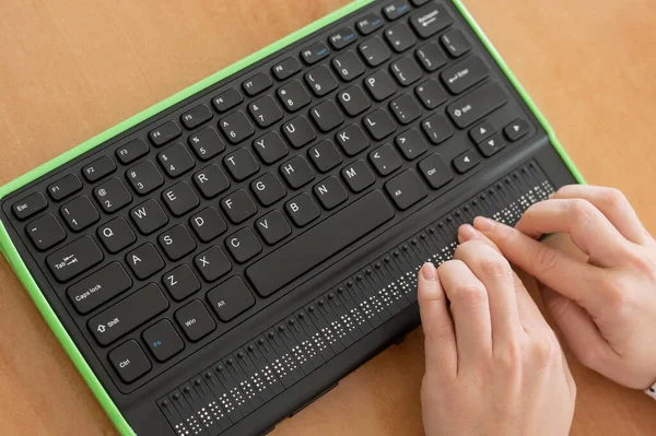 Uma mulher cega usa um computador com um monitor Braille e um teclado de computador. Dispositivo inclusivo. — Fotografia de Stock
