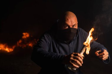 Maskeli bir adam yanan bir şişe tutuyor. Molotof kokteyli.