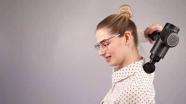 Lächelnde Frau mit Zahnspange benutzt Massagepistole für den Rücken. — Stockfoto