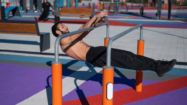 Póló nélküli férfi vízszintes egyensúlyt csinál párhuzamos rúdakon a sportpályán. — Stock Fotó