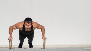 Siyah spor kıyafetli bir adam dışarıda ring şınavı çekiyor..