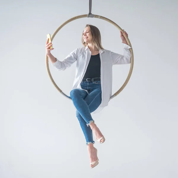 Caucasian woman gymnast on an aerial hoop takes a selfie on a smartphone.
