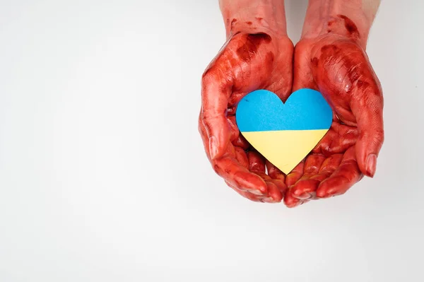 Femme avec les mains couvertes de sang tenant un cœur avec le drapeau de l'ukraine sur un fond blanc. — Photo