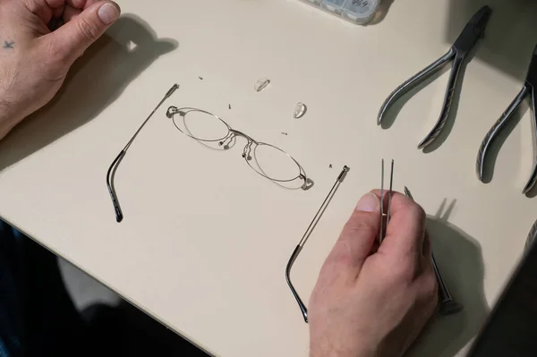 Un uomo ripara una montatura rotta di occhiali. Primo piano delle mani oftalmologi — Foto Stock