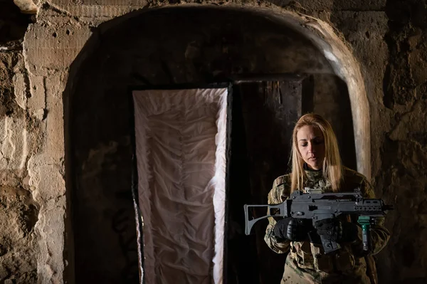 Blanke vrouw in legeruniform die een machinegeweer vasthoudt en bij een open kist staat. — Stockfoto